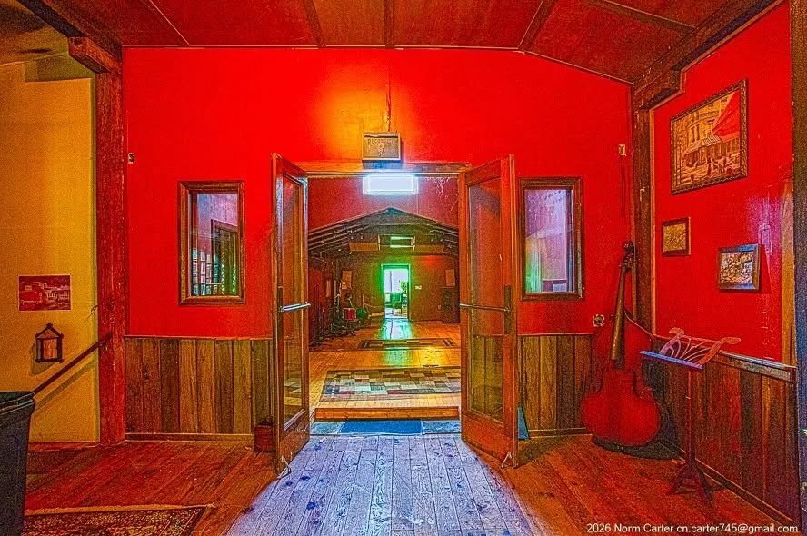 The entry hall: deep red walls, wood wainscot, double doors standing open toward the performance hall, a red upright bass leaning by the doorway.